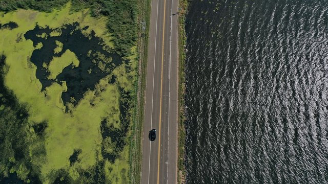 Car on Road Over Lake Algae & Water on Each Side (Drone)