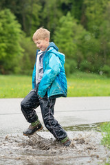 Junge in Regenkleidung springt in Wasserpfütze