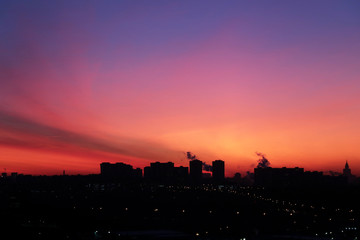 Sunrise over the city, scenic view with night lights. Pink-blue sky and cirrus clouds in soft colors above black silhouettes of high-rise buildings, colorful cityscape for background
