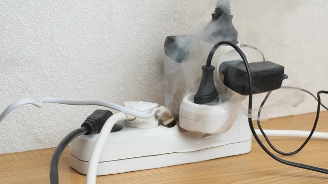 power strip smoking from overload by electrical appliances on table in room in close-up. concept of occurrence of fire.