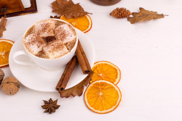 Cup of coffee with marshmallows and cocoa, leaves, dried oranges, spices, on a white background. Delicious hot autumn drink, morning mood. Copy space.