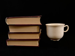 Naklejka premium Closed books and a cup of coffee on a black background. A cup of tea and a hardcover book.