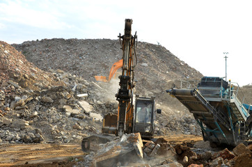 Fototapeta premium Salvaging and recycling building and construction materials. Excavator with hydraulic hammer work at landfill with concrete demolition waste. Reinforced concrete mobile shredder. Reuse concrete