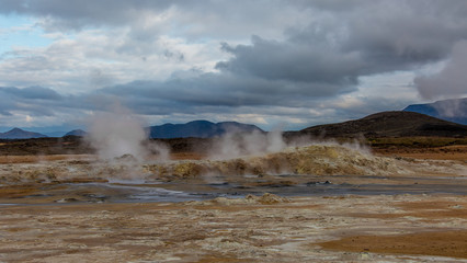 View of volcanic active terrain with white vapor coming out of the ground and water
