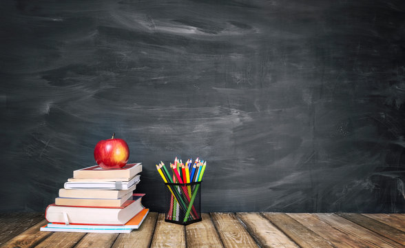 The concept of education, stack of books, an apple, pencils against the background of the school blackboard
