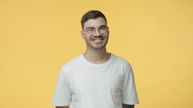 Studio portrait young caucasian guy in white t-shirt, glasses, smiling pleased, hearing good idea, nod in agreement and like, give positive answer, say yes lets travel, standing yellow background