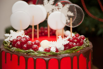 Close up Christmas red cake with chocolate smudges, decorated red currant, candy and lollipops and Christmas tree on the background