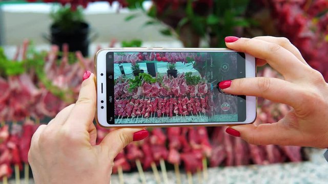 A woman photographs on the smartphone rows of delicious raw lamb for a barbecue or grill. Social network blogger concept photo.
