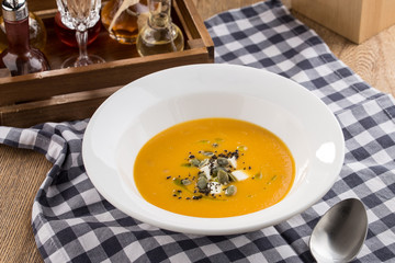 Pumpkin cream soup with seeds on fabric napkin on wooden table