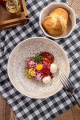 Appetizer Steak Tartare with bread bun and yolk on fabric napkin on wooden table