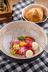 Appetizer Steak Tartare with bread bun and yolk on fabric napkin on wooden table