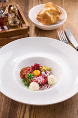 Appetizer Steak Tartare with bread bun and yolk on white plate on wooden table