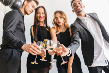 Indoor portrait of joyful man with big smile celebrating birthday with friends. Photo of ladies and gentlemen clink wineglasses on important event.