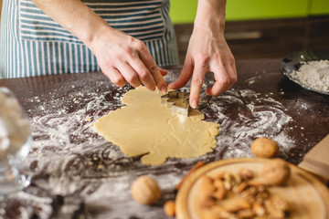Cook housewife making Christmas cookies at home on a colorful kitchen. Hands making dough the shape of Christmas trees