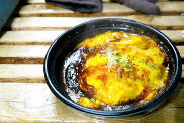 Omelet with cheese and sauce on rice in black take away bowl