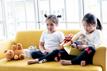 A 6 and 4 year old Asian girl Sitting on yellow sofa, are happiness and excited Because received a...