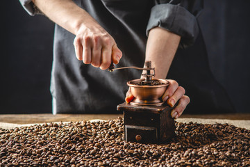 Hands baristas in a dark apron grind on a manual grinder fragrant coffee beans. Selection of fresh coffee for espresso