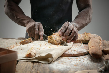 Close up of african-american man slices fresh cereal, white bread, bran with a kitchen knife on wooden table. Healthy eating, nutrition, craft product. Gluten-free food, vegan lifestyle, organic taste