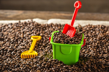 Children's toys a bucket with a shovel on a pile of roasted coffee beans like in sandbox. Harm of caffeine for children