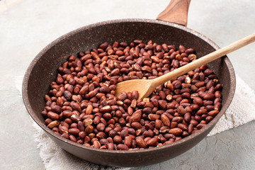 Roasted peanuts in a pan on a light gray textured background.