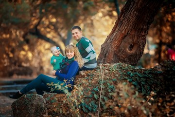 Family with baby mom and dad sitting under a tree in the forest and happines together.