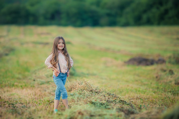 A girl of 8-9 years old walks on an agricultural field on the background of a dense green forest.