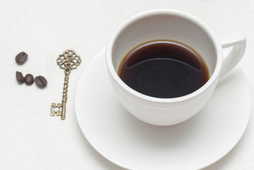 White tea cup with black coffee and golden key on white background.