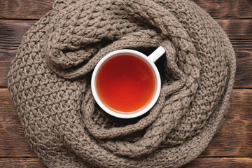 Cup of hot tea and warm scarf on wooden table background.