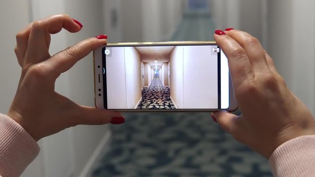 A woman is holding a smartphone and photographing the corridor at the hotel.