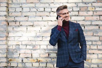 Fototapeta na wymiar Smiling businessman talking on smartphone with brick wall at background