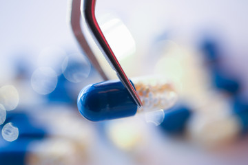 Arm lifting up pill with tweezers closeup