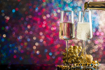 Two glasses of champagne surrounded by Christmas decorations on a background of multi-colored lights.