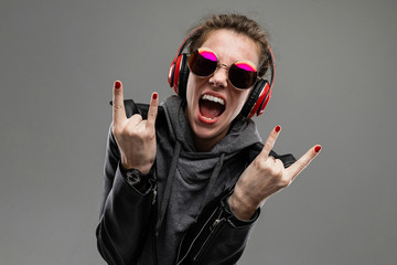 smiling impudent girl in rocker style listens to music in red headphones on a gray background