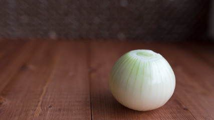 Peeled fresh onions on a wooden background. The contrast is white and brown. A whole onion without golden husks. Place for text.