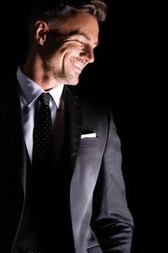 Businessman in formal wear looking down and smiling isolated on black