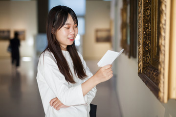 Chinese woman with guide-book near picture collection in the museum