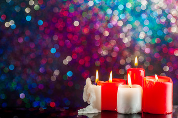 Burning candles surrounded by Christmas decorations on a background of multi-colored lights.