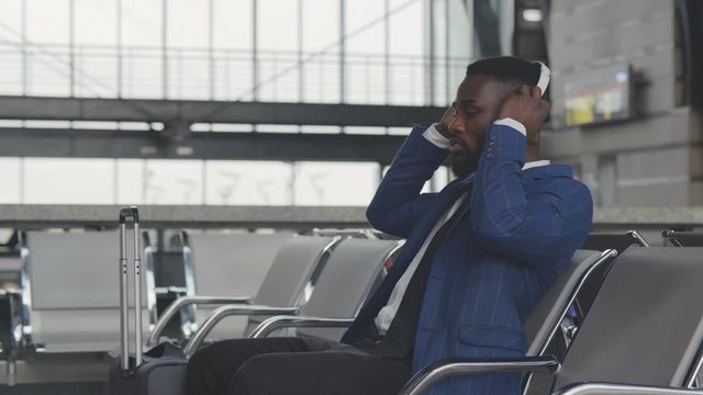 Yung businessman in headphones waiting for train or flight in waiting area