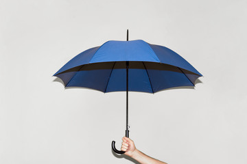 A man holds a blue umbrella in his hand against a gray wall. Concept autumn, color of the year 2020, business, protection