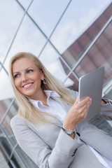 Happy businesswoman looking away while holding digital tablet against office building