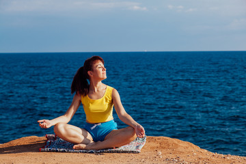 the girl is engaged in yoga sits on the cliff by the sea