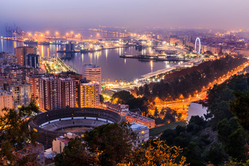 Naklejka premium Panoramic view at night from Malaga on the Spanish Mediterranean coast. City view on the Costa del Sol with illuminated harbor, residential buildings, trees, street lamps, ferris wheel, ships