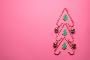 Christmas tree figure made of sweets and decorative balls on a pink background, top view