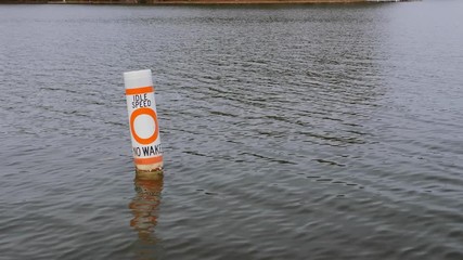 No wake safety buoy on lake alerting boaters to idle speed restriction. Nautical warning caution float on freshwater reservoir.