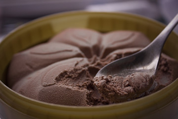 A bucket of chocolate ice cream with a spoon. Spoon took the ice cream with the taste of chocolate. Beautiful ice cream pattern.