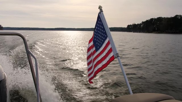 American stars and stripes flag waving from flag pole on stern of pleasure boat while cruising on fresh water lake. 