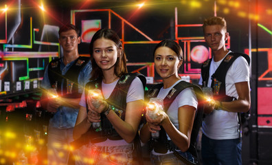 Fototapeta na wymiar Smiling young women standing with guns during laser tag game wit