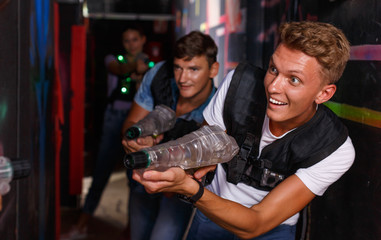 Young guy holding colored laser guns and took aim during laser tag game in labyrinth