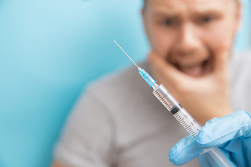 Man is fear and cries from syringe with vaccination doctor appointment. Concept trypanophobia