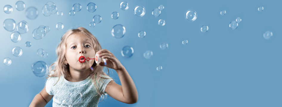 Cute girl with curly hair blowing bubbles on blue background